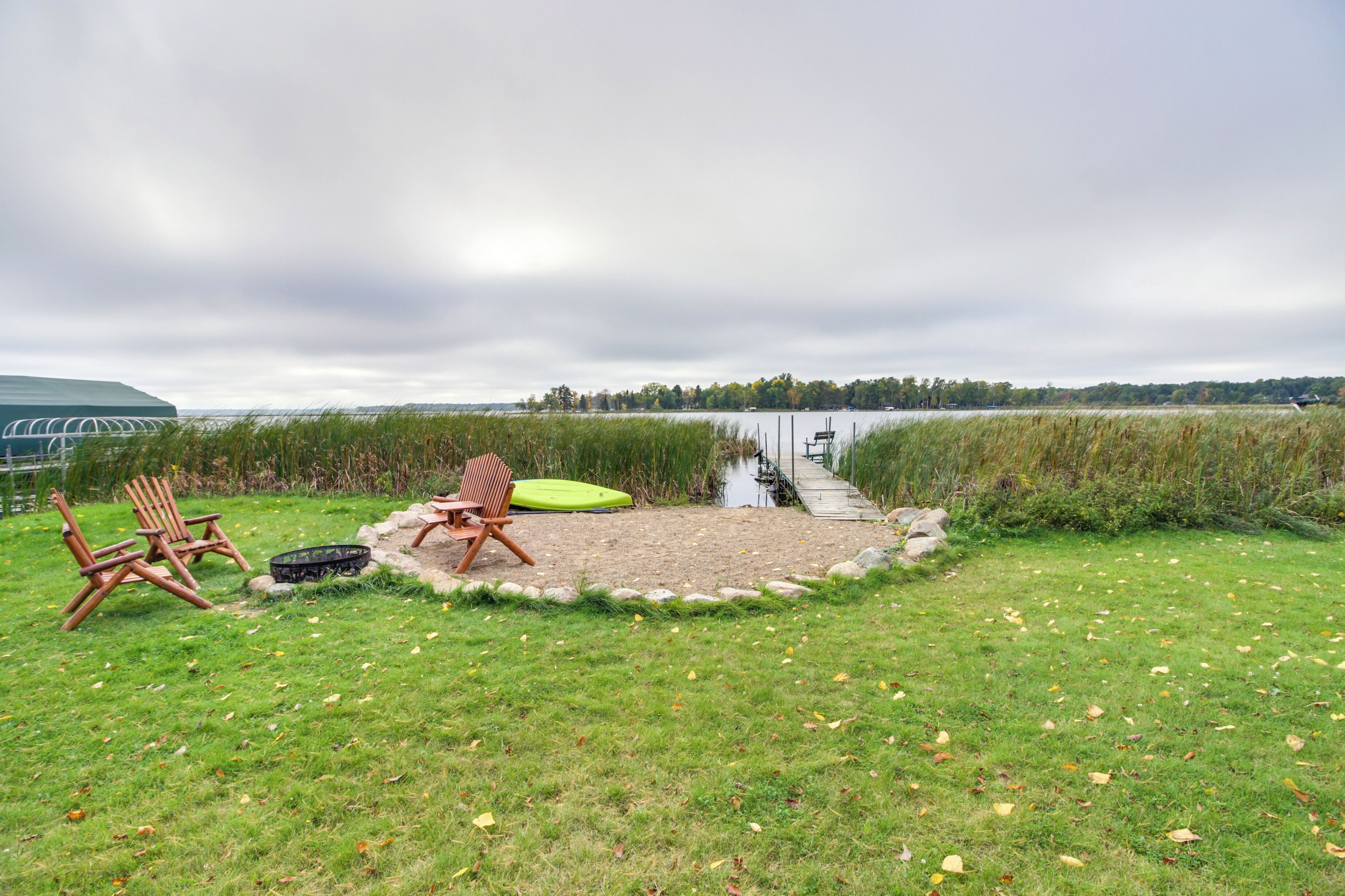 A lakeside setting with a grassy area, two wooden chairs, and a green mat.