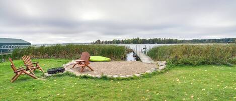 A lakeside setting with a grassy area, two wooden chairs, and a green mat.