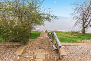 A pathway leading to a beach with a wooden fence and a tree on the left. - Deck + Fire Pit: Waterfront Lake Michigan Escape (Algoma)