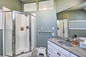 Un baño con cabina de ducha de vidrio, tocador con lavamanos y un espejo grande.