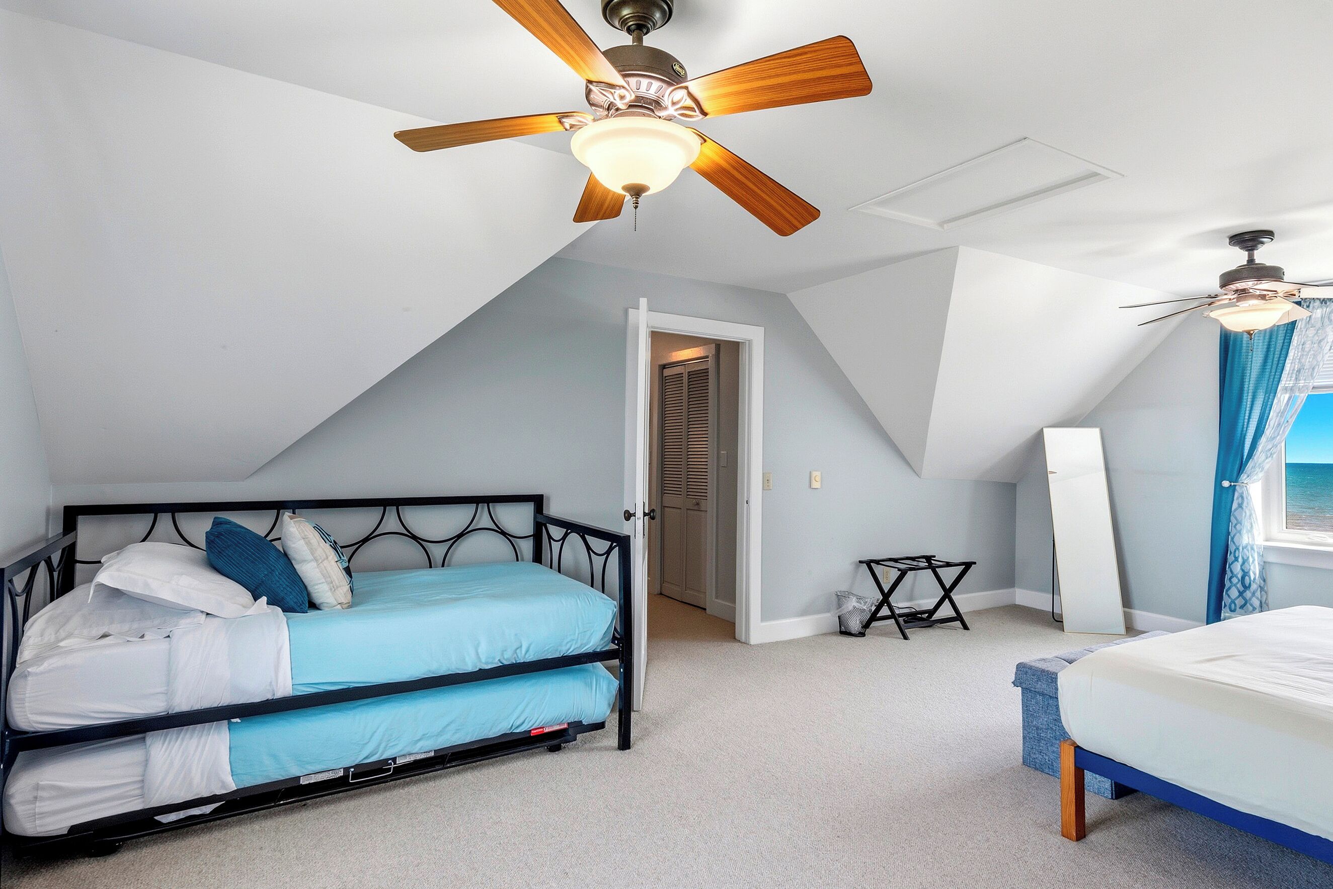A bedroom with a bed, a desk, a ceiling fan, and a window with curtains.