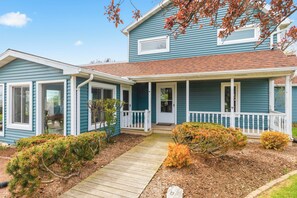 A two-story house with a front porch, a covered entryway, and a small front yard with mulch and shrubs. - Deck + Fire Pit: Waterfront Lake Michigan Escape (Algoma)