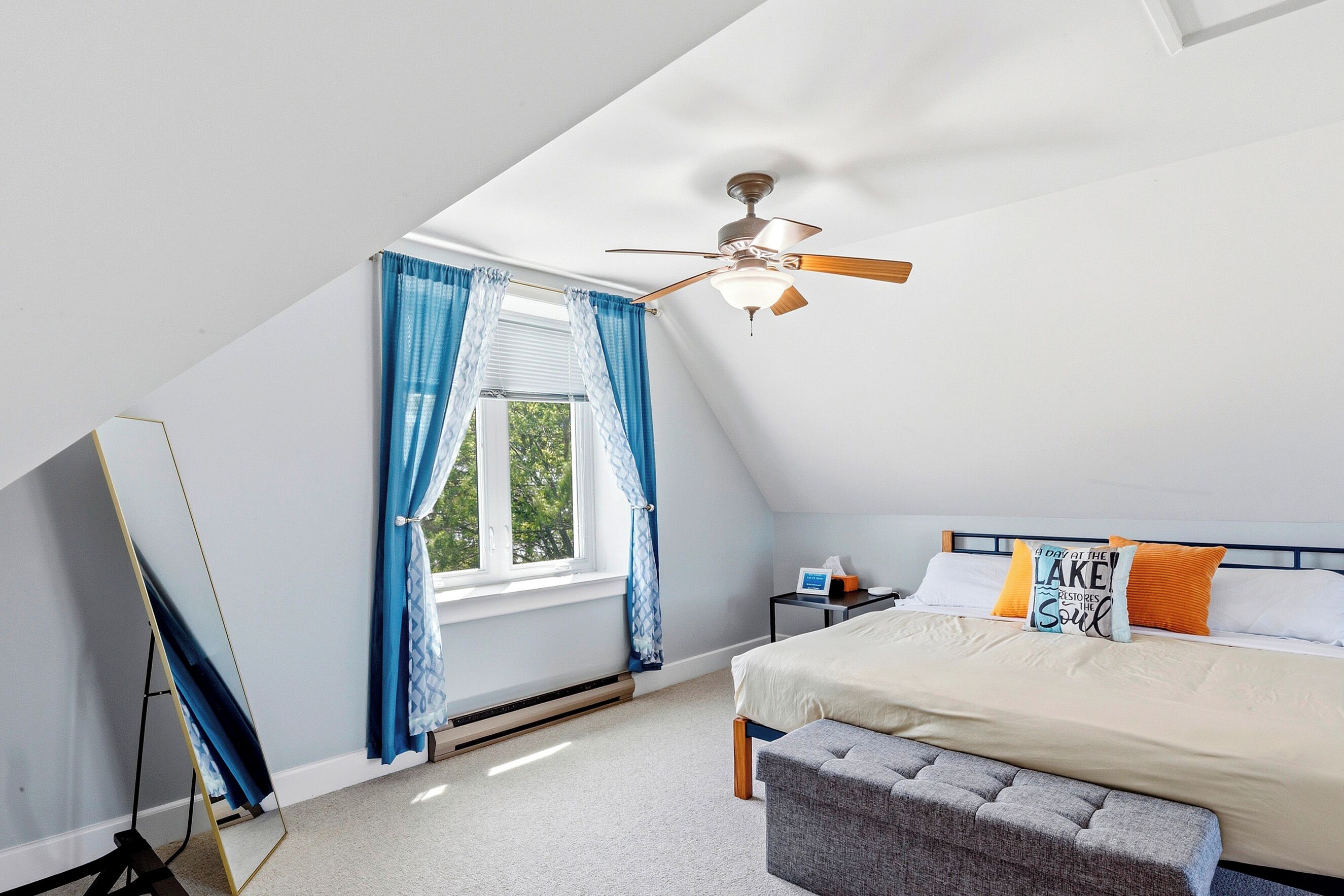 A bedroom with a sloped ceiling, a bed with pillows, a bedside table, and a window with curtains.