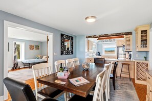 A spacious dining area with a wooden table, white chairs, and a view into the kitchen. - Deck + Fire Pit: Waterfront Lake Michigan Escape (Algoma)