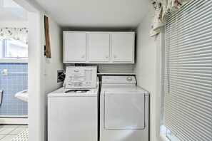 A laundry area with a front-loading washer and dryer, a cabinet above, and a window with blinds. - Deck + Fire Pit: Waterfront Lake Michigan Escape (Algoma)