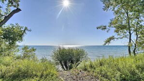 A pathway leading to a body of water, surrounded by greenery and trees. - Deck + Fire Pit: Waterfront Lake Michigan Escape (Algoma)