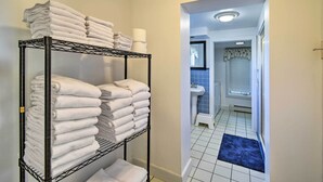 A hallway with a metal rack holding folded white towels and a blue mat leading to a bathroom with a sink and blue tiles. - Deck + Fire Pit: Waterfront Lake Michigan Escape (Algoma)