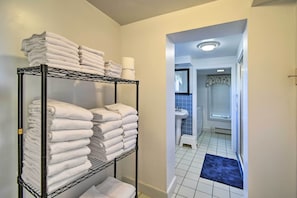 Un pasillo con un perchero metálico que sostiene toallas blancas dobladas y un tapete azul que conduce a un baño con lavamanos y azulejos azules.