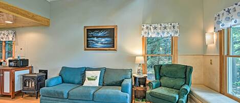 A cozy living room with a blue sofa, a green armchair, a wooden table with a microwave, and a painting on the wall.