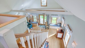 Un loft spacieux avec de hauts plafonds, des poutres en bois, un escalier et une vue sur l’extérieur.