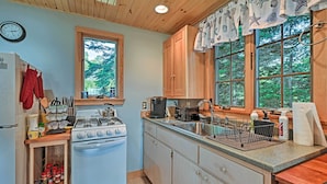 A kitchen with wooden cabinets, a stove, and a window with curtains. - Charming Stonington Studio w/ Ocean Views! (Stonington)