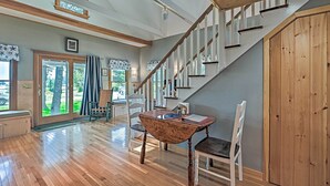 Une pièce spacieuse avec un plancher en bois, une table à manger avec des chaises, un escalier et une grande fenêtre avec des rideaux.