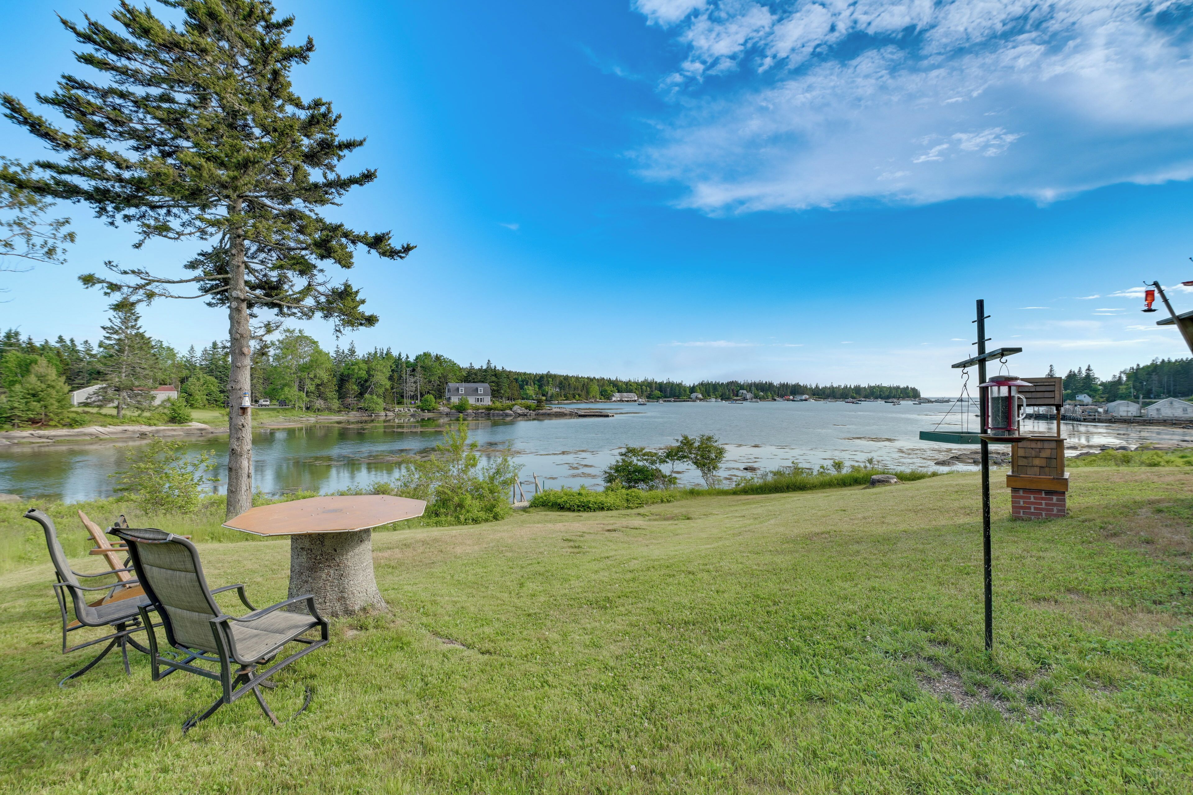 Ett utomhusområde vid sjön med bord och stolar, omgivet av gräs och träd.