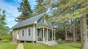 Une petite maison à un seul étage, dotée d’un porche et entourée d’arbres et d’une pelouse.