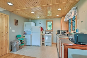 A compact kitchen with wooden ceiling, white appliances, and a window with a view of greenery.