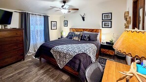 Une chambre à coucher comprenant un lit, un ventilateur de plafond, une commode, un bureau avec une lampe et une tête de cerf fixée au mur.