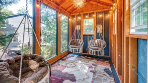 A cozy room with large windows, wooden beams, and hanging chairs. - Hot Tub, Beach Access: Albrightsville Retreat! (Albrightsville)