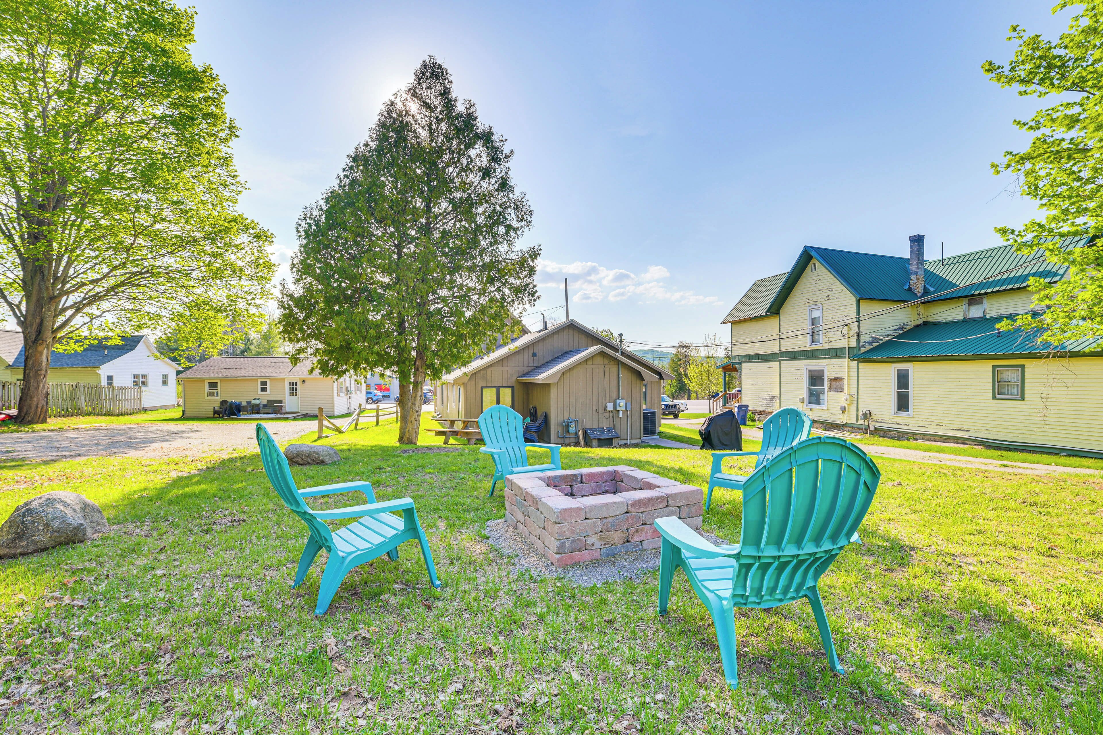 Un espace extérieur verdoyant, avec un foyer et des fauteuils Adirondack turquoise.