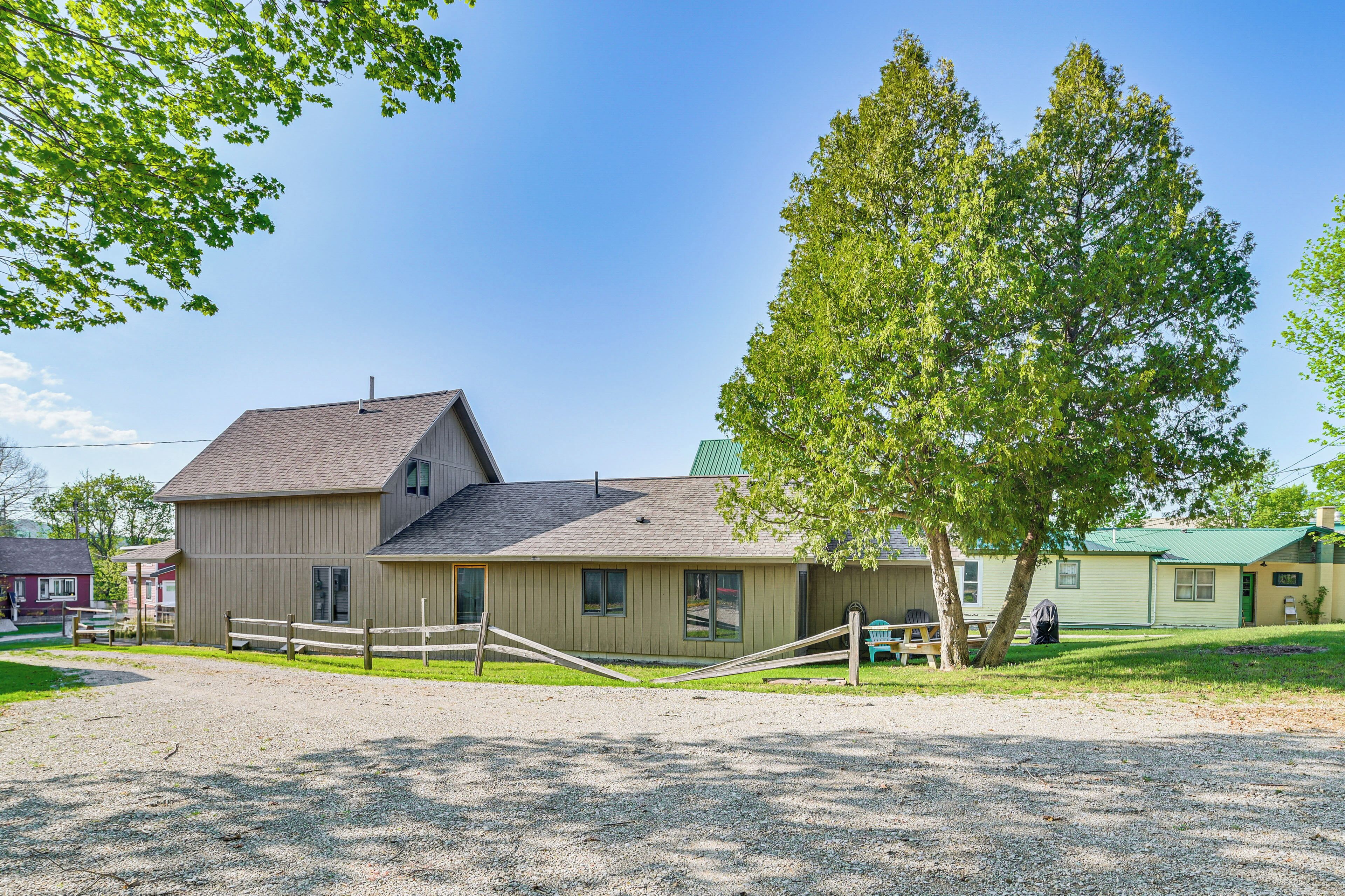 A stable with a fenced area, a large tree, and a building with a green roof.