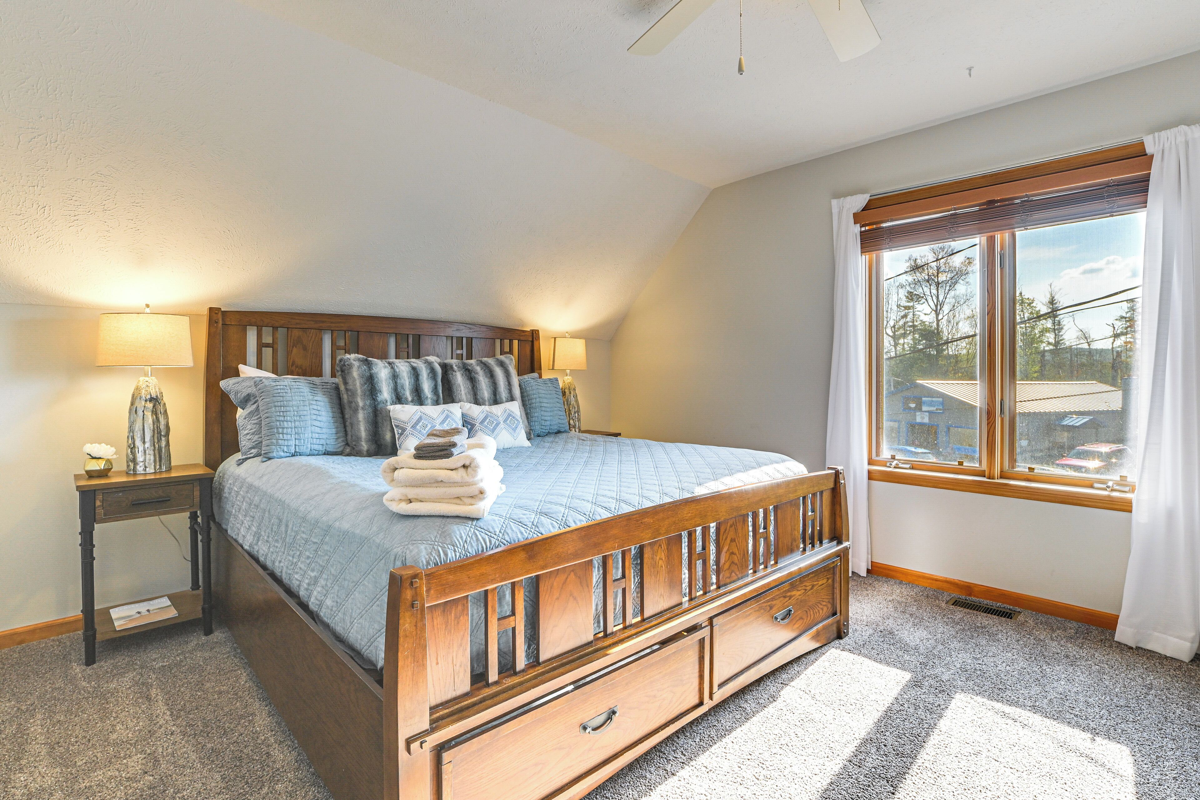 A bedroom with a wooden bed, a nightstand, a lamp, and a window with curtains.