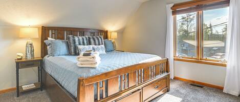 A bedroom with a wooden bed, a nightstand, a lamp, and a window with curtains.