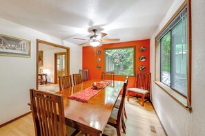 Una sala da pranzo con un tavolo in legno, sedie, una ventola a soffitto e un'ampia finestra vista verde.