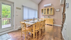 A dining area with a wooden table and chairs, a window with blinds, a cabinet with glass doors, and a small plant on the wall.