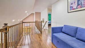 A spacious room with a wooden staircase, a blue sofa, and a framed artwork on the wall.