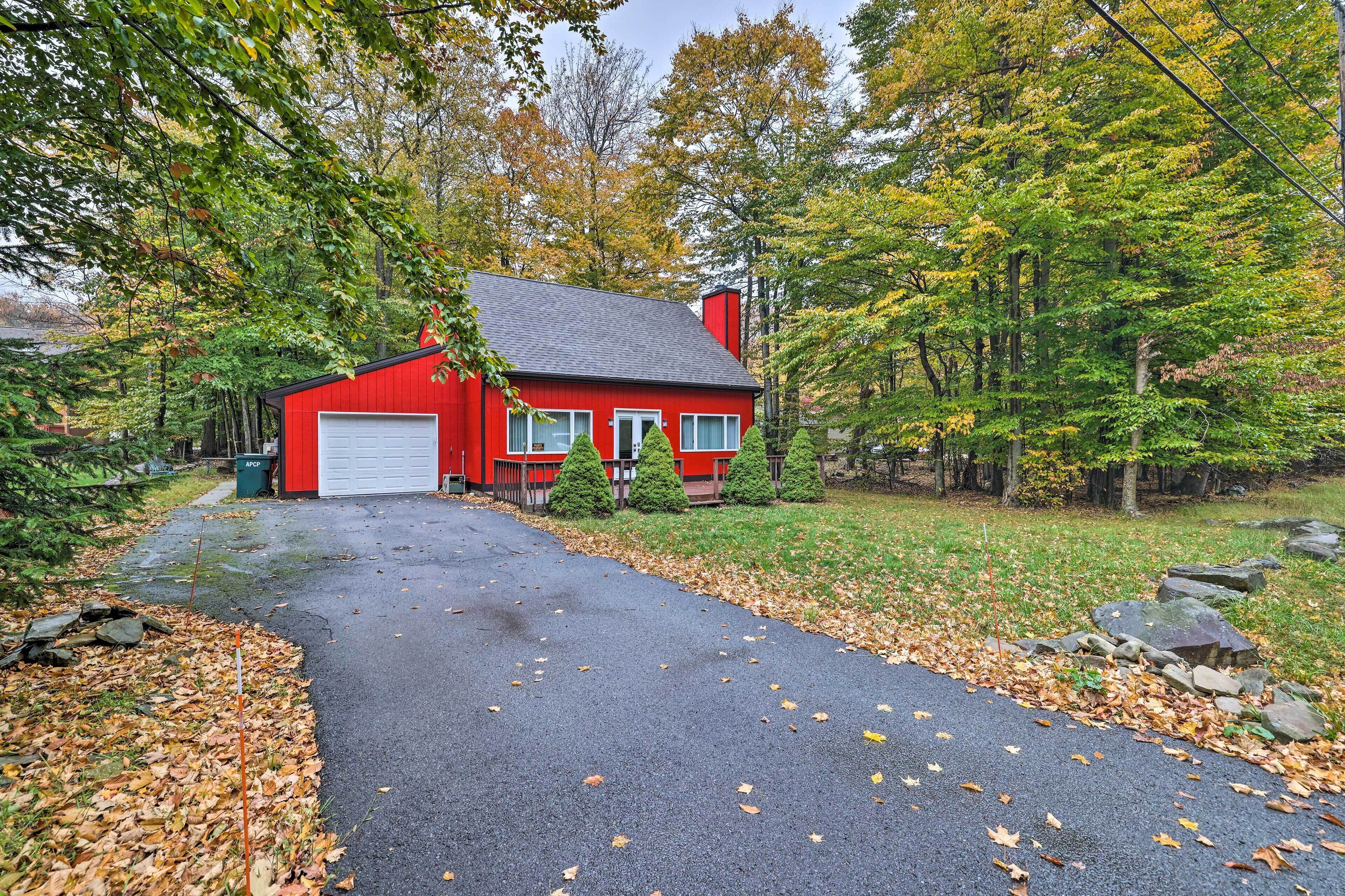 A red house with a garage, surrounded by trees and a driveway.