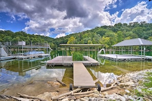 A dock extending into a calm lake with a forested hillside in the background.