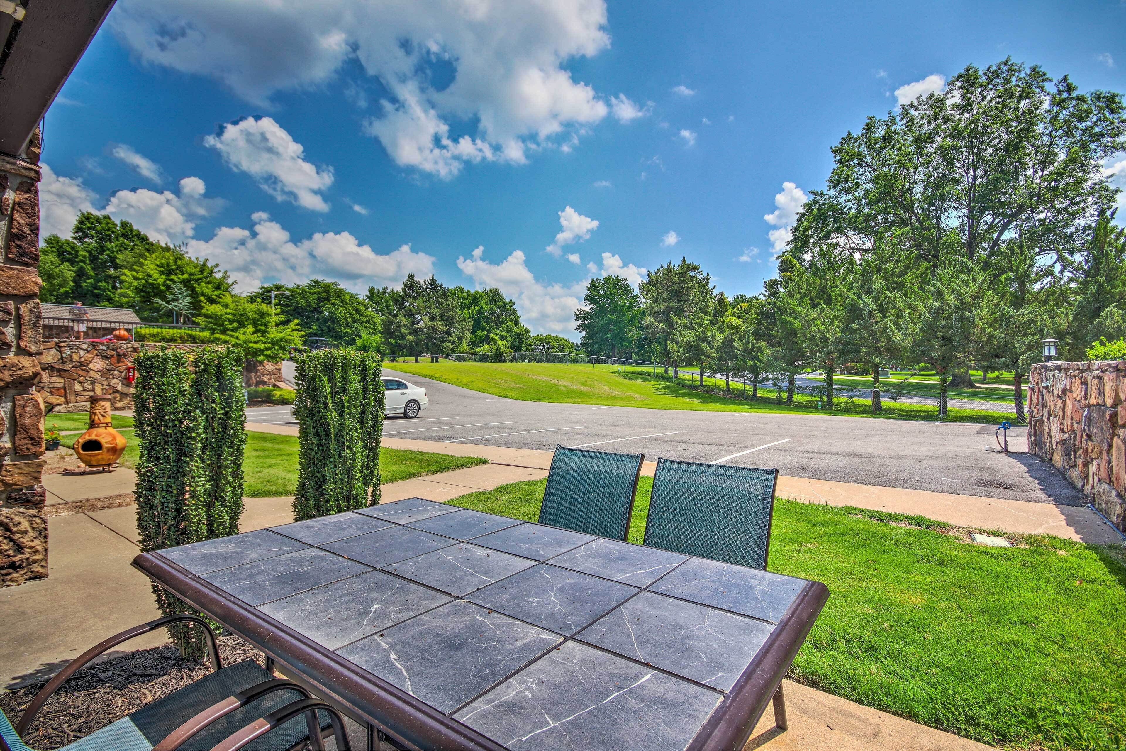 Un patio con una mesa y sillas de piedra, con vista a una carretera y un campo de golf.