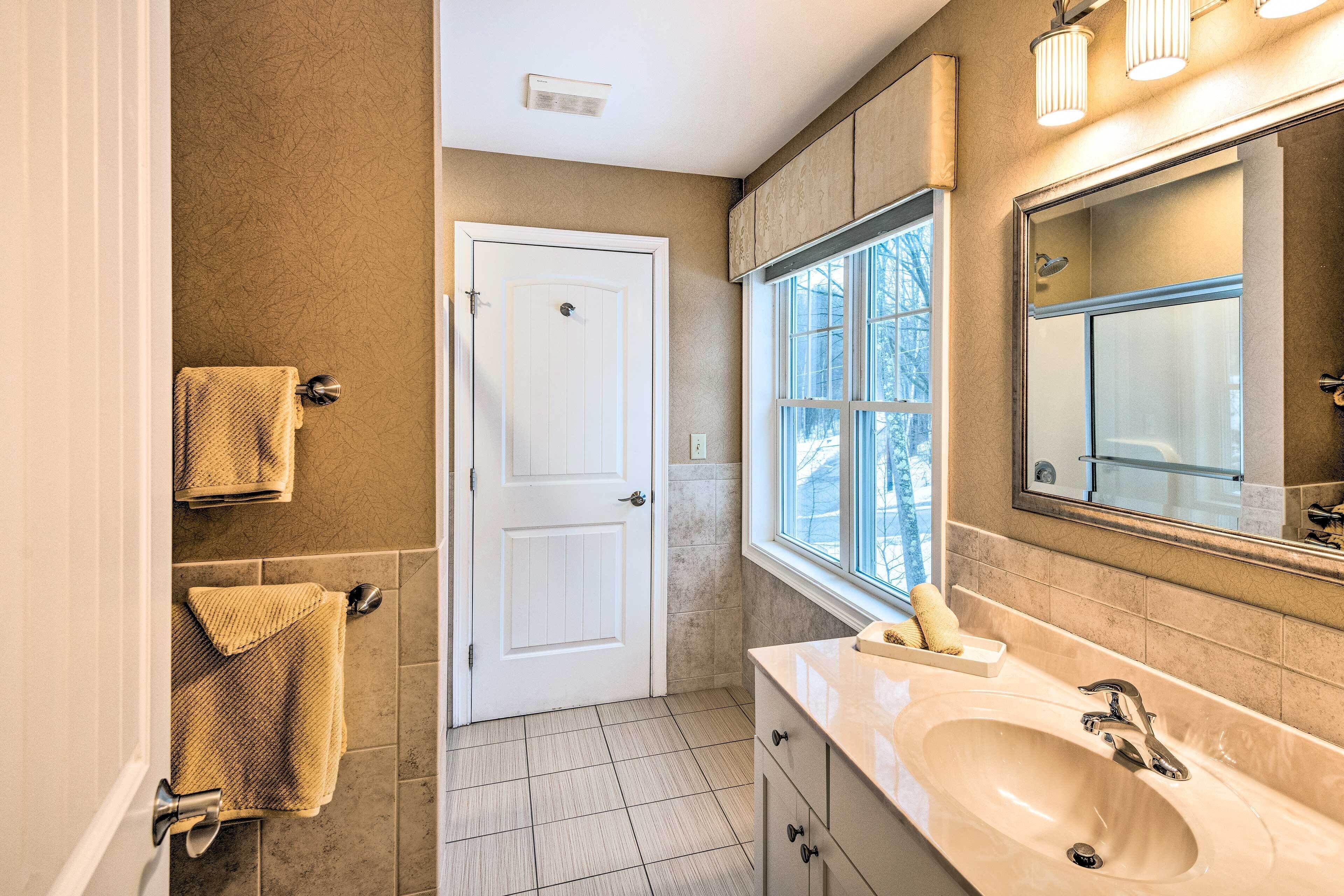 A bathroom with a white door, beige walls, a large mirror, a sink, and a window.