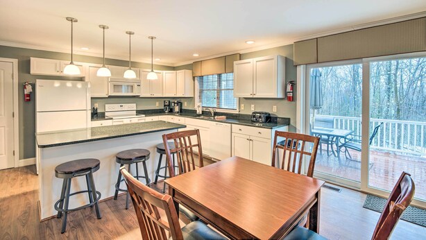 A modern kitchen with white cabinets, a wooden dining table, and bar stools.
