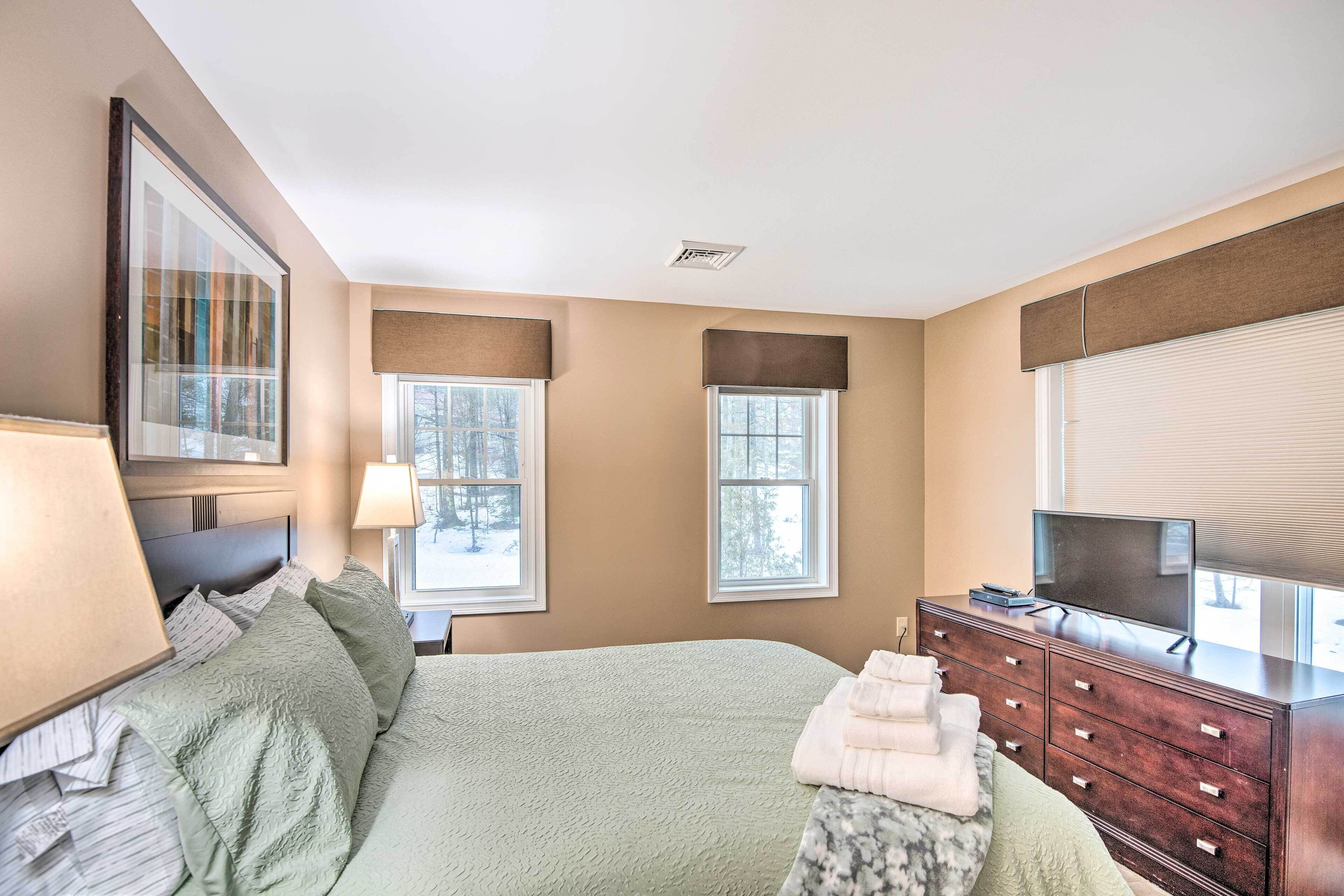 A bedroom with a bed, dresser, TV, and windows.