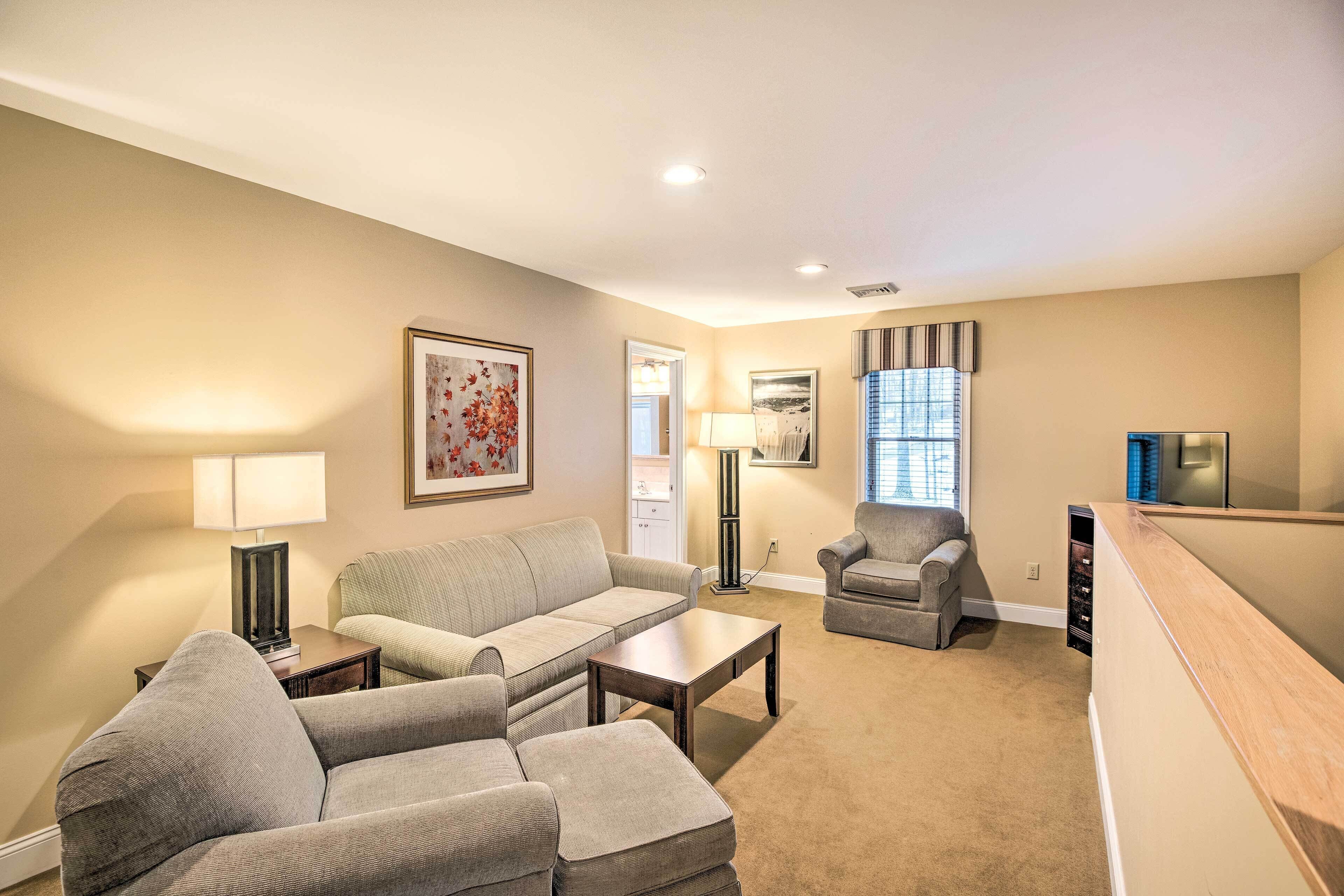 A living room with a beige carpet, a grey sofa, a coffee table, a floor lamp, and a television.