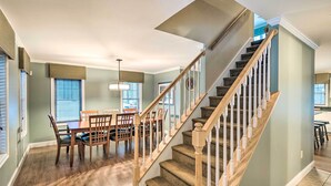A dining area with a wooden table and chairs, a staircase with wooden railings, and a light fixture above the table.