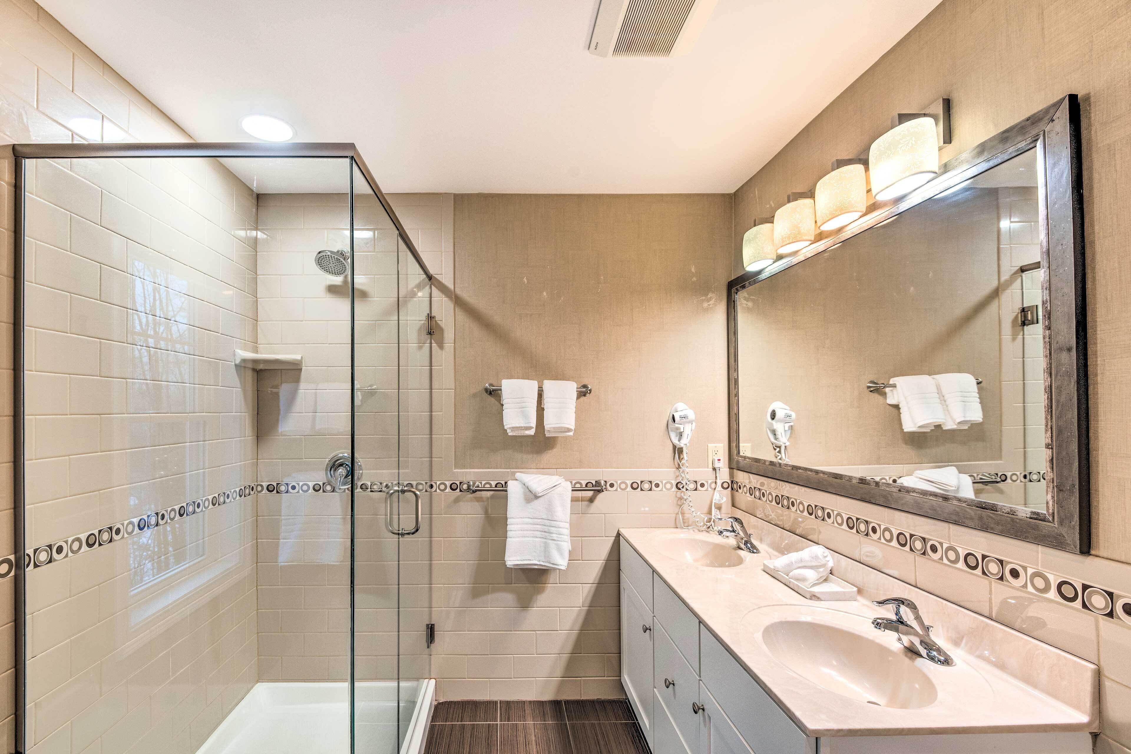 A modern bathroom with a glass shower enclosure, a vanity with a sink, and a large mirror.