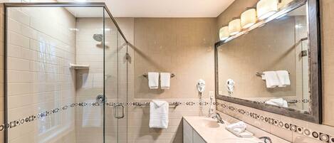 A modern bathroom with a glass shower enclosure, a vanity with a sink, and a large mirror.