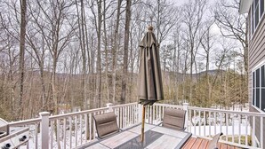 A deck with a table and chairs, surrounded by a white railing, overlooking a snowy landscape with trees.
