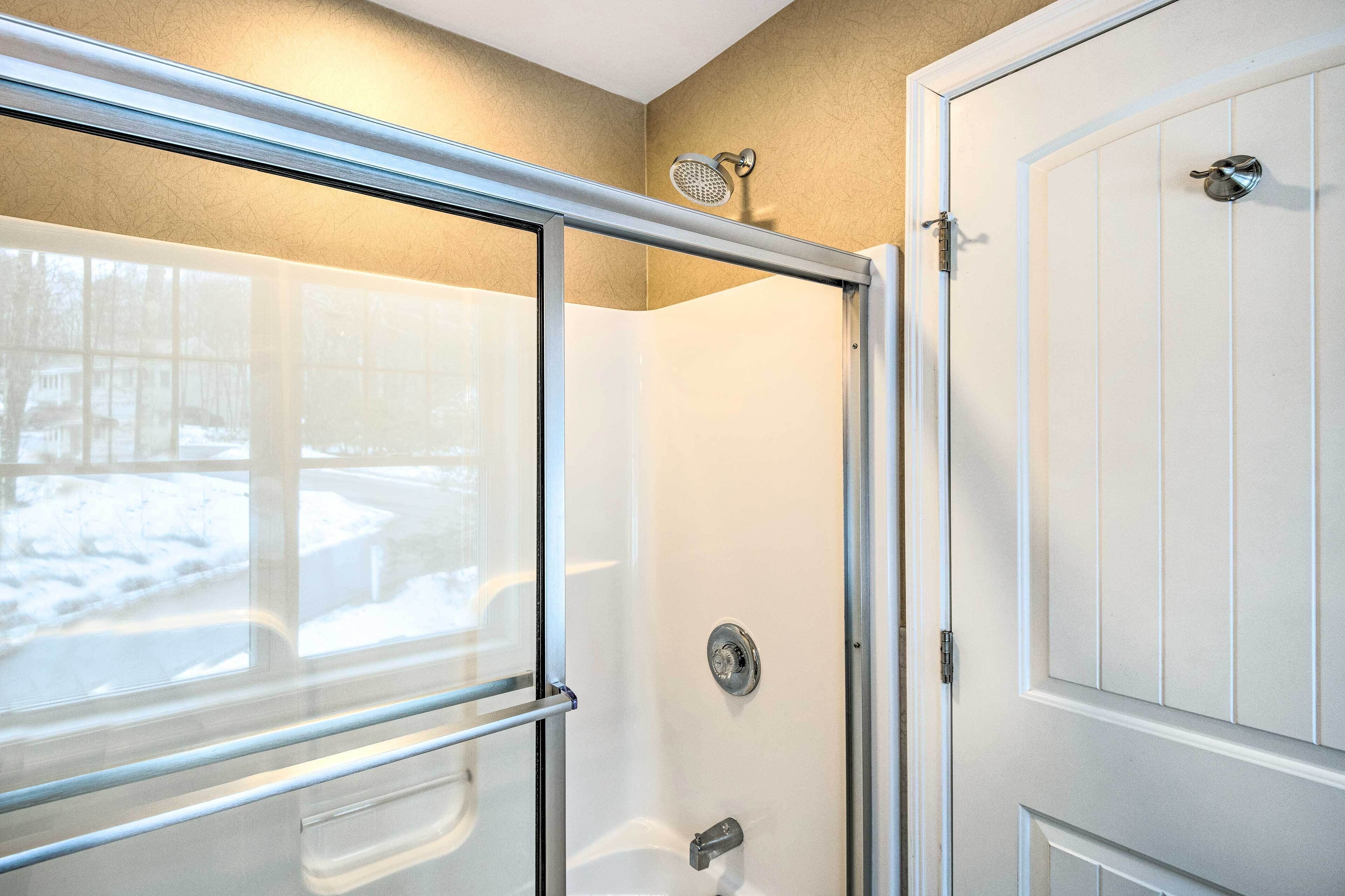 A shower with a glass door, a showerhead, and a toilet visible through the glass.