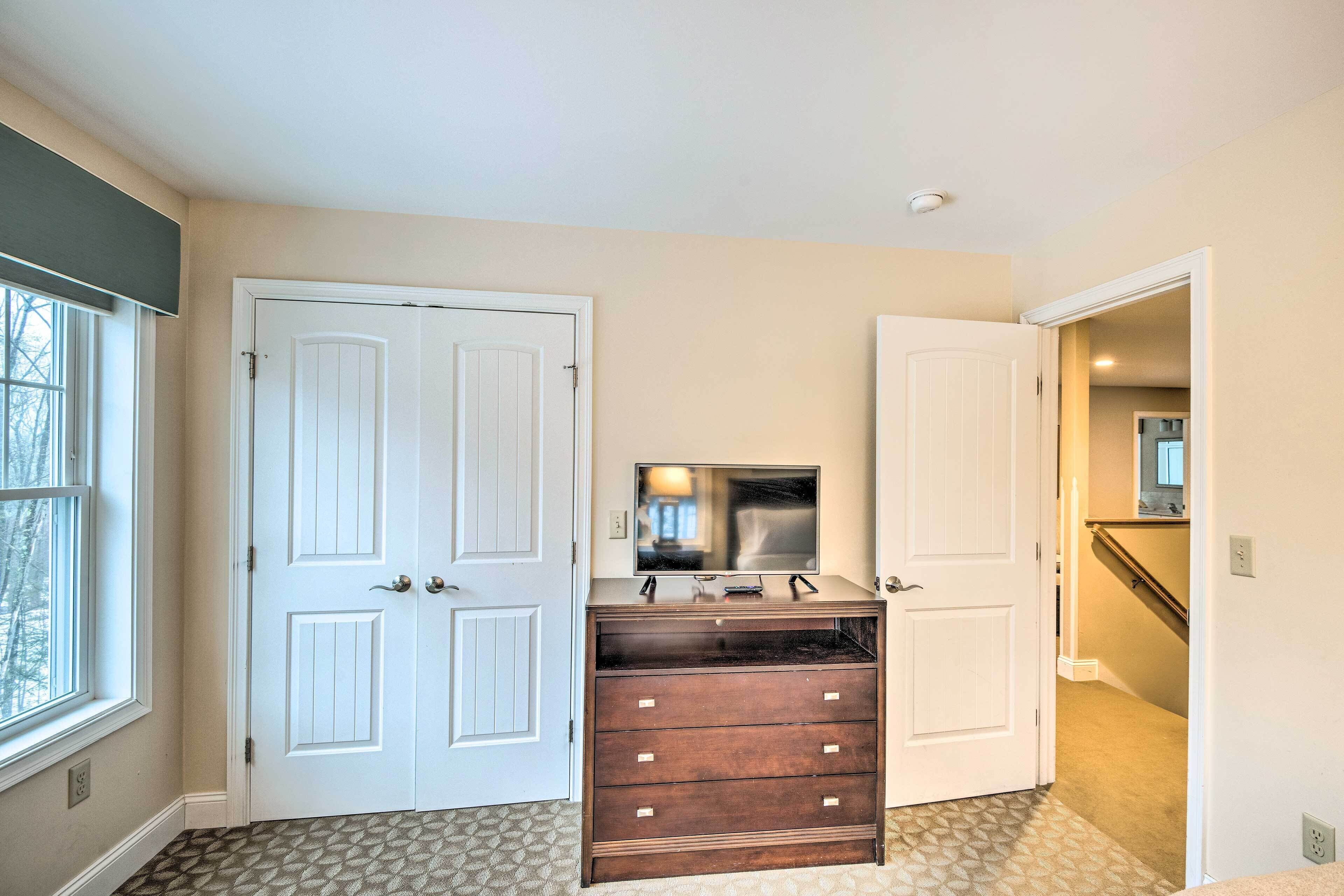 A room with two white doors, a dark wooden dresser, a flat-screen TV on top, and a patterned carpet.