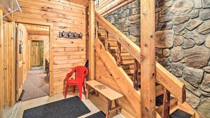 Interieur van een houten blokhut met een stenen muur, een houten trap en een rode stoel.