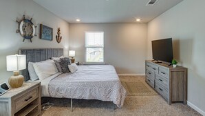 A bedroom with a bed, a dresser, a TV, a window, and decorative wall art. - 'camden Ocean Springs' House Near Beaches! (Ocean Springs)