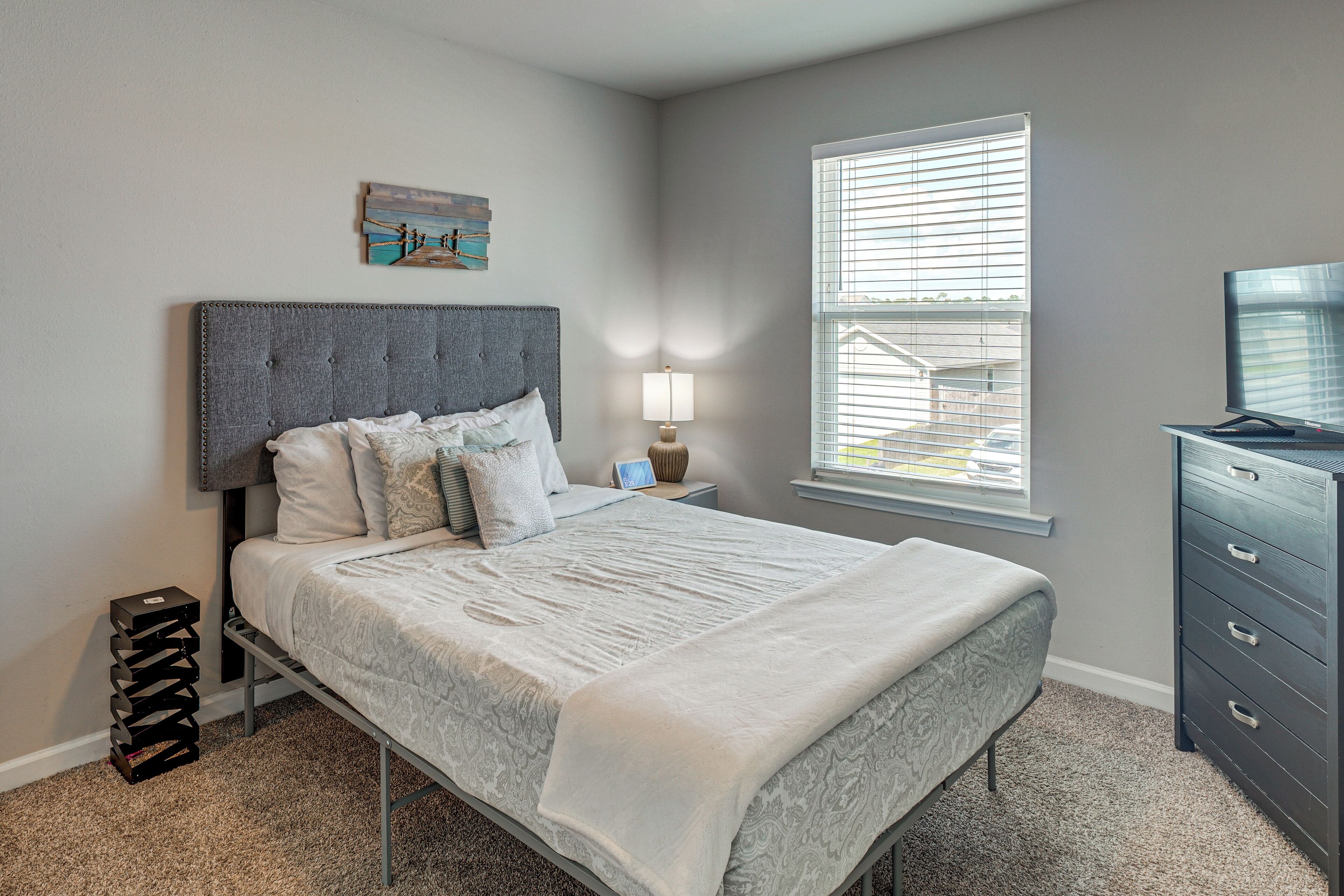 A bedroom with a bed, a nightstand, a lamp, a dresser, and a window with blinds.