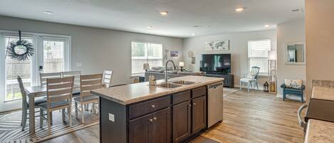 A spacious kitchen with a large island, wooden flooring, and a dining area with chairs and a table.