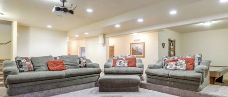 A living room with a gray sectional sofa, ottoman, and a ceiling-mounted projector.