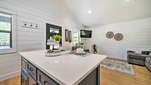 Una cocina moderna con una isla grande, piso de madera y un sofá gris en la sala de estar.