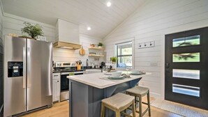 Una cocina moderna con un refrigerador de acero inoxidable, una isla central con taburetes, armarios de madera y una puerta negra con paneles de vidrio esmerilado.