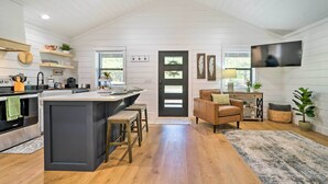 Una cocina moderna con una isla central, taburetes de bar y un comedor con sofá y mesa de centro.