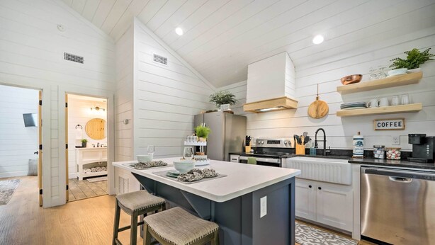Una cocina moderna con una isla central, electrodomésticos de acero inoxidable, taburetes de bar de madera y un letrero de café en la pared.